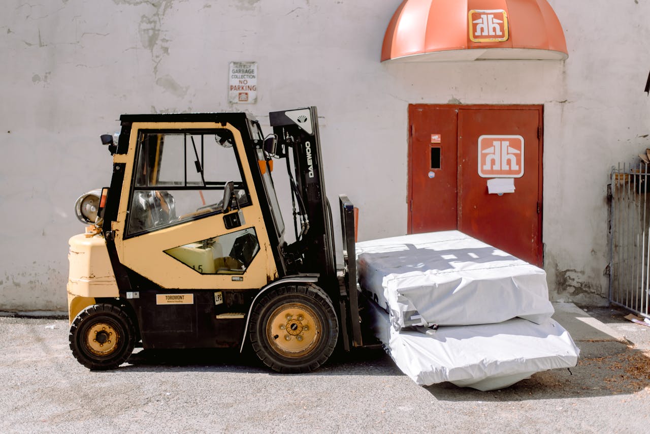 services-01 Forklift unloading wrapped goods outside an industrial building with a red door.
